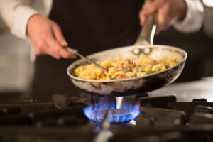 cook preparing pasta dish with vegetables on stove.